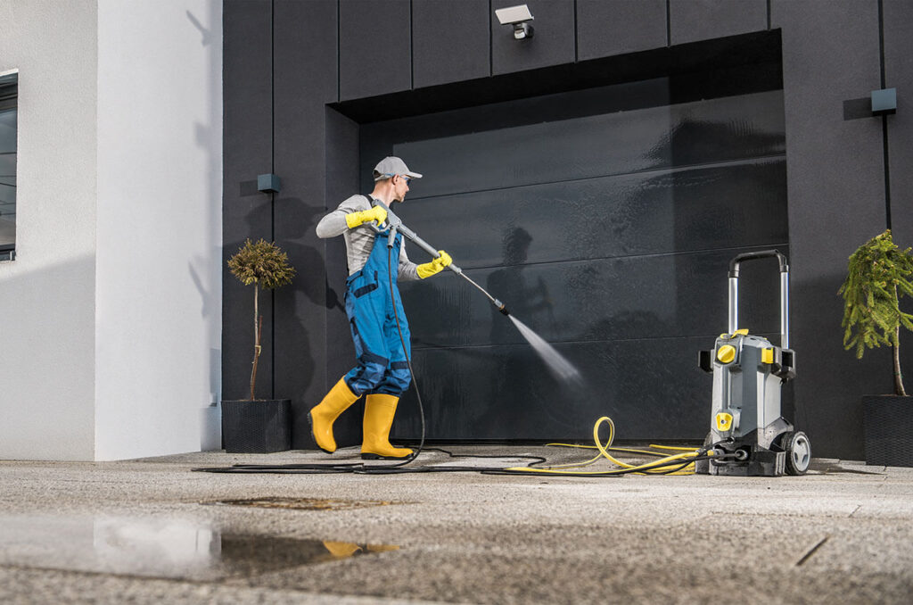 Pressure washing professional in action, using a high-pressure washer system to clean a large garage door.