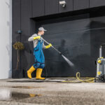 Pressure washing professional in action, using a high-pressure washer system to clean a large garage door.