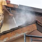 Expert performing house washing with a pressure washer on a roof.